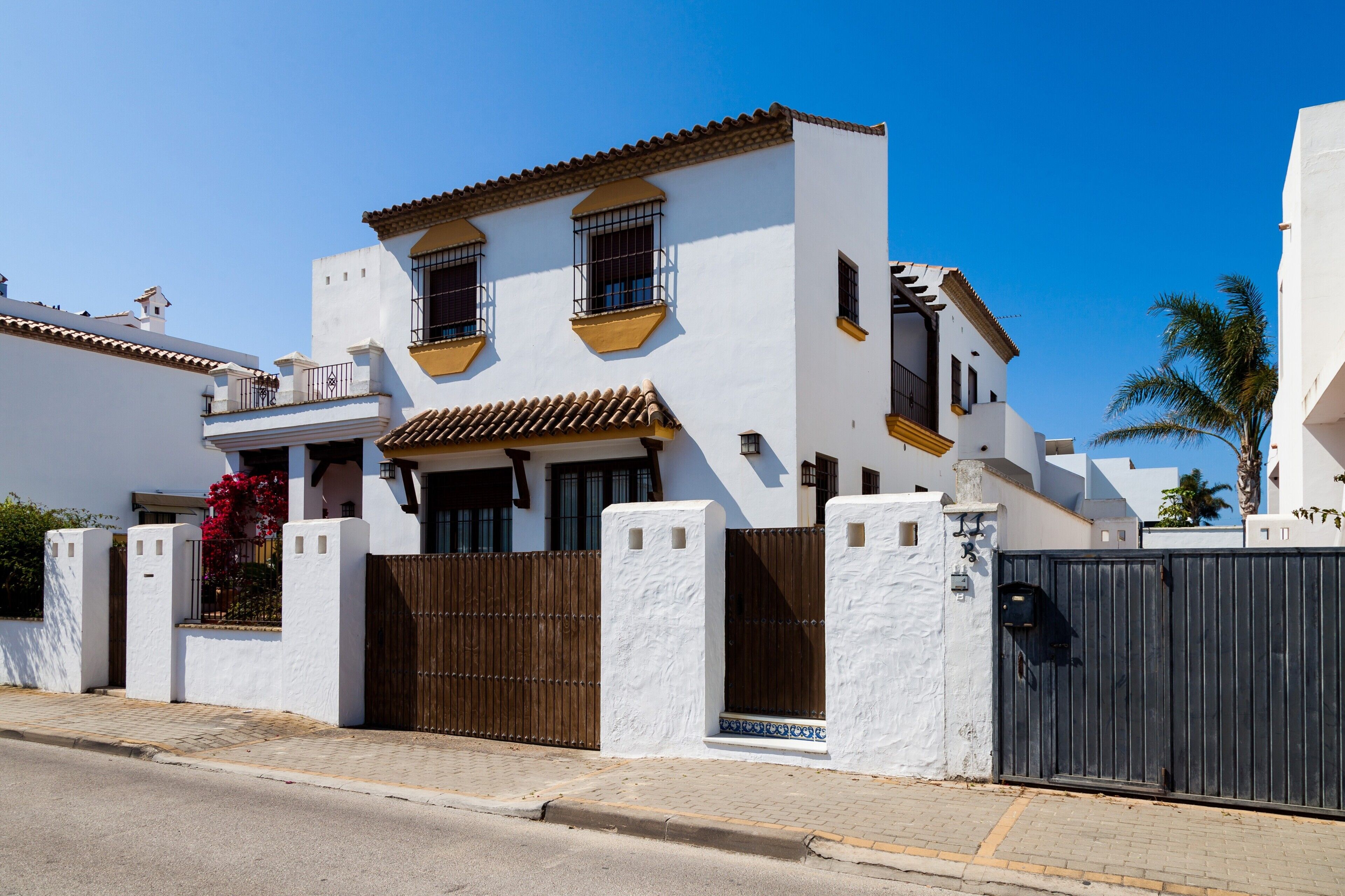 A white building with a brown gate, a balcony, and a clear blue sky.