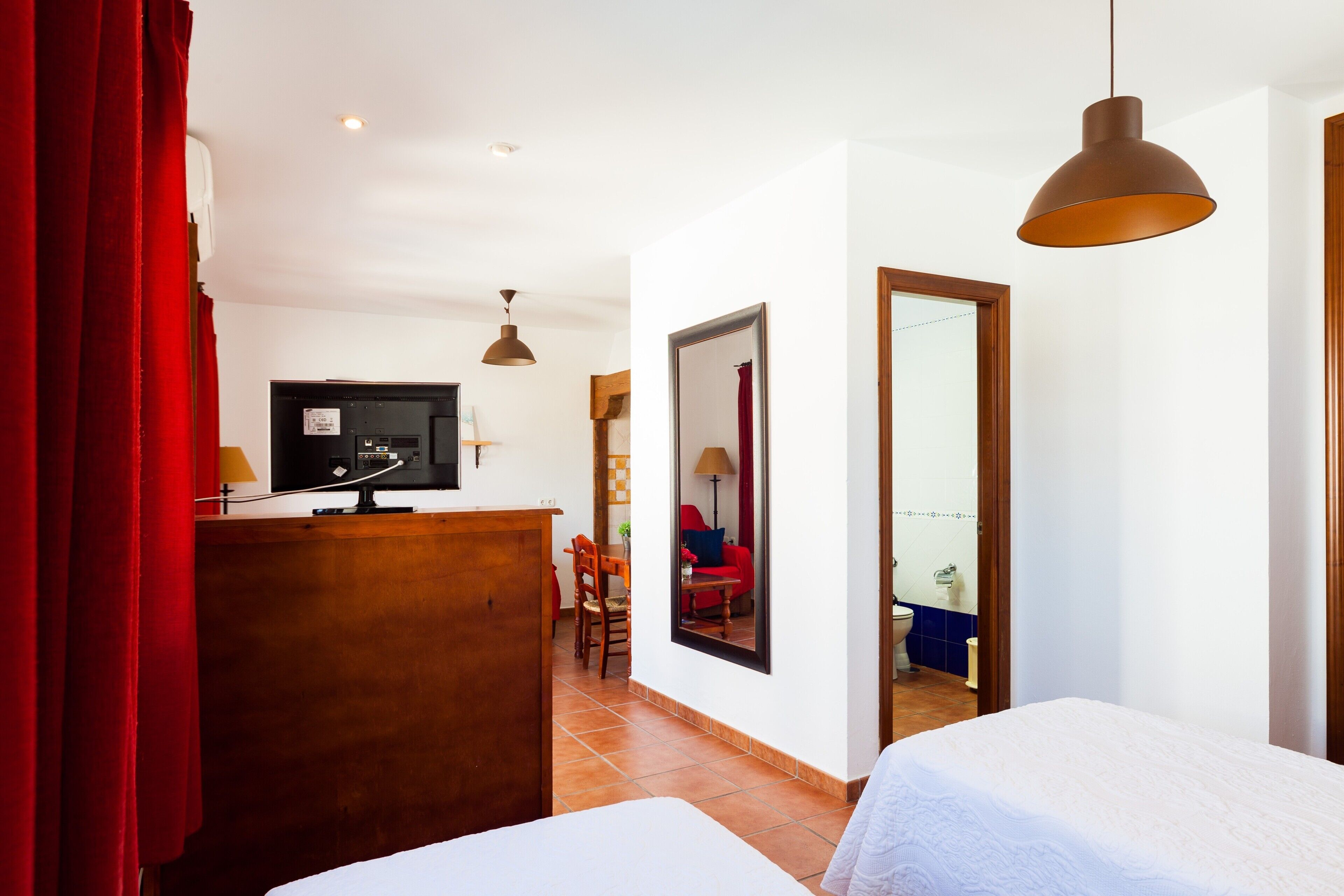 Une chambre d’hôtel avec un lit, un bureau avec une télévision, une chaise, un miroir et un rideau rouge.
