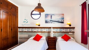 Una habitación con dos camas, un armario de madera, una lámpara de pared, un velero decorativo y una pintura de faro.