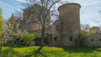 A historic building with a courtyard, a large tree, and a small building in the foreground.