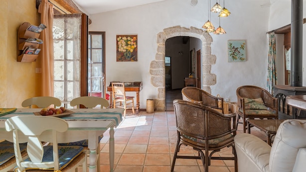 Un interior rústico con comedor, mobiliario de mimbre, un arco de piedra y chimenea.