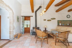 Un interior rústico con paredes de piedra, vigas de madera, piso de baldosas, muebles de mimbre, chimenea y un reloj en la pared.