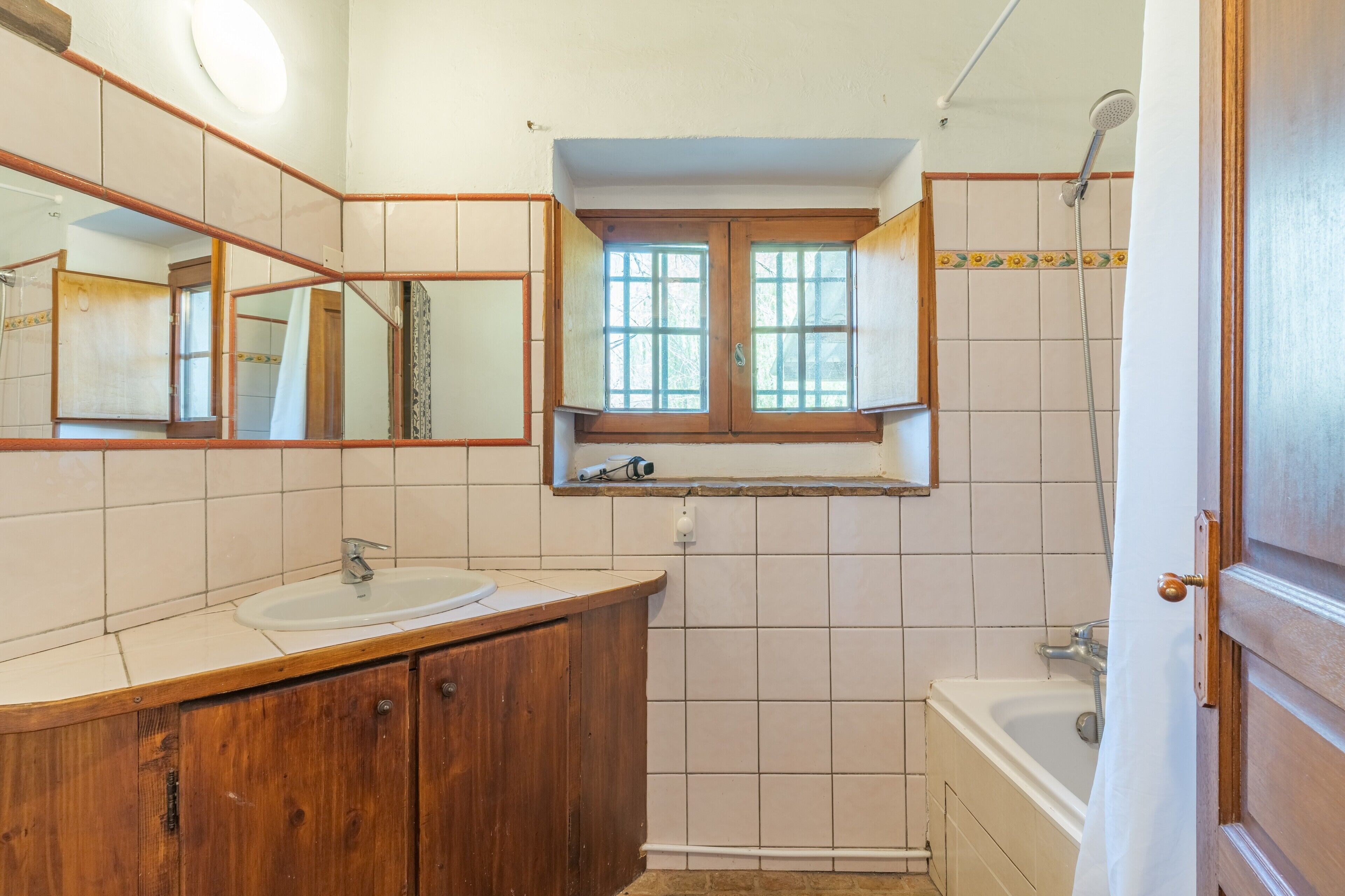 Une salle de bain avec un meuble-lavabo en bois, un évier, une fenêtre et une douche.