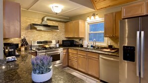 Una cocina moderna con encimeras de granito, electrodomésticos de acero inoxidable, armarios de madera y un ventanal que ofrece luz natural.