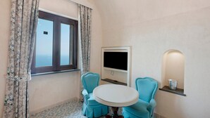 A room with a window, a flat-screen TV, a round table, two chairs, a shelf with a pot, and patterned floor tiles. - Holiday Home 'Dimora Elegante In Costa D'Amalfi' with Sea View, Wi-Fi and Air Conditioning (Conca dei Marini)