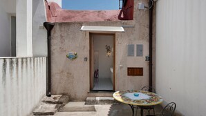 A narrow outdoor space with a door leading to an interior, a small table with chairs, and a wall-mounted light fixture. - Holiday Home 'Dimora Elegante In Costa D'Amalfi' with Sea View, Wi-Fi and Air Conditioning (Conca dei Marini)