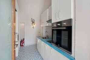 Uma cozinha compacta com armários brancos, bancada azul, pia de aço inoxidável e forno preto.