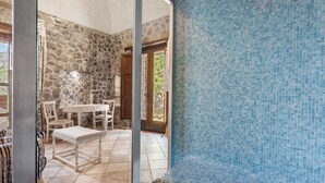 A room with a stone wall, tiled floor, a dining table with chairs, and a blue tiled wall.