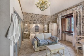 Una habitación con pared de piedra, un sofá, una mesa, un armario y una ventana con cortinas.