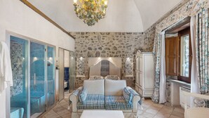 A room with a stone wall, a sofa, a table, a chandelier, and a shower area.