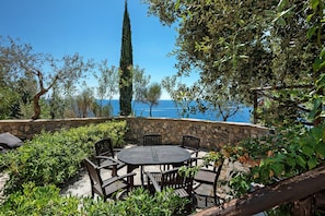 An outdoor seating area with a stone wall, a round table, and chairs, overlooking a body of water.