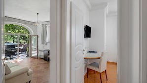 Une pièce comprenant une table à manger, une chaise, un téléviseur fixé au mur et une porte-fenêtre coulissante donnant sur un espace extérieur avec une terrasse.