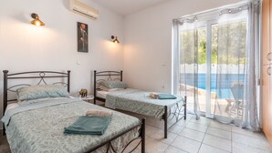 Quarto com duas camas, uma mesa pequena e uma cadeira. Há uma janela com vista para uma piscina e uma cerca.