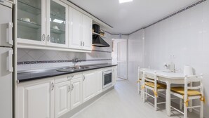 Eine Küche mit weißen Schränken, einer schwarzen Arbeitsplatte und einem Essbereich mit weißem Tisch und Stühlen.