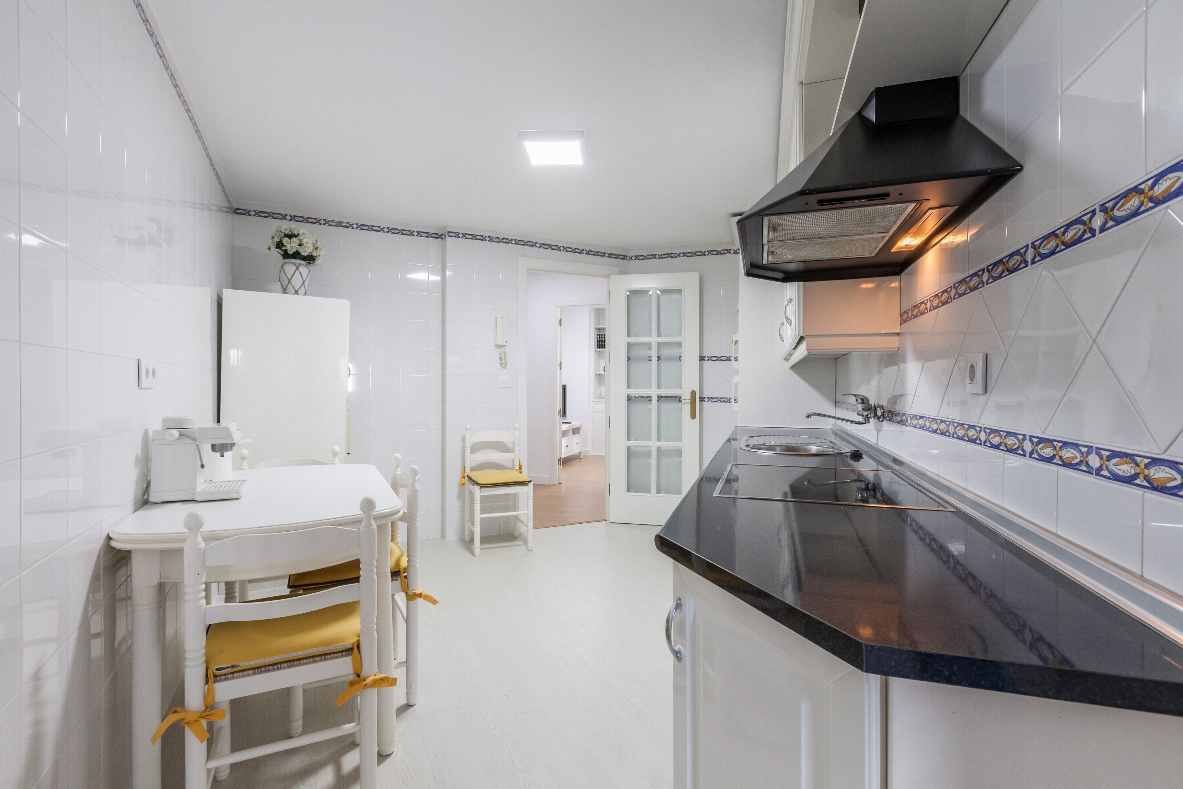 Une cuisine avec des meubles blancs, un plan de travail noir et une table à manger blanche avec des chaises.