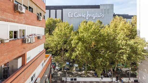 Ein Gebäude mit einem Schild, auf dem 'El Corte Inglés' steht, und einem Innenhof mit Bäumen und geparkten Autos.