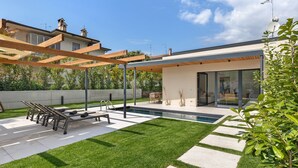 Ein modernes Haus mit Swimmingpool, Sitzgelegenheit im Freien und einer Pergola.
