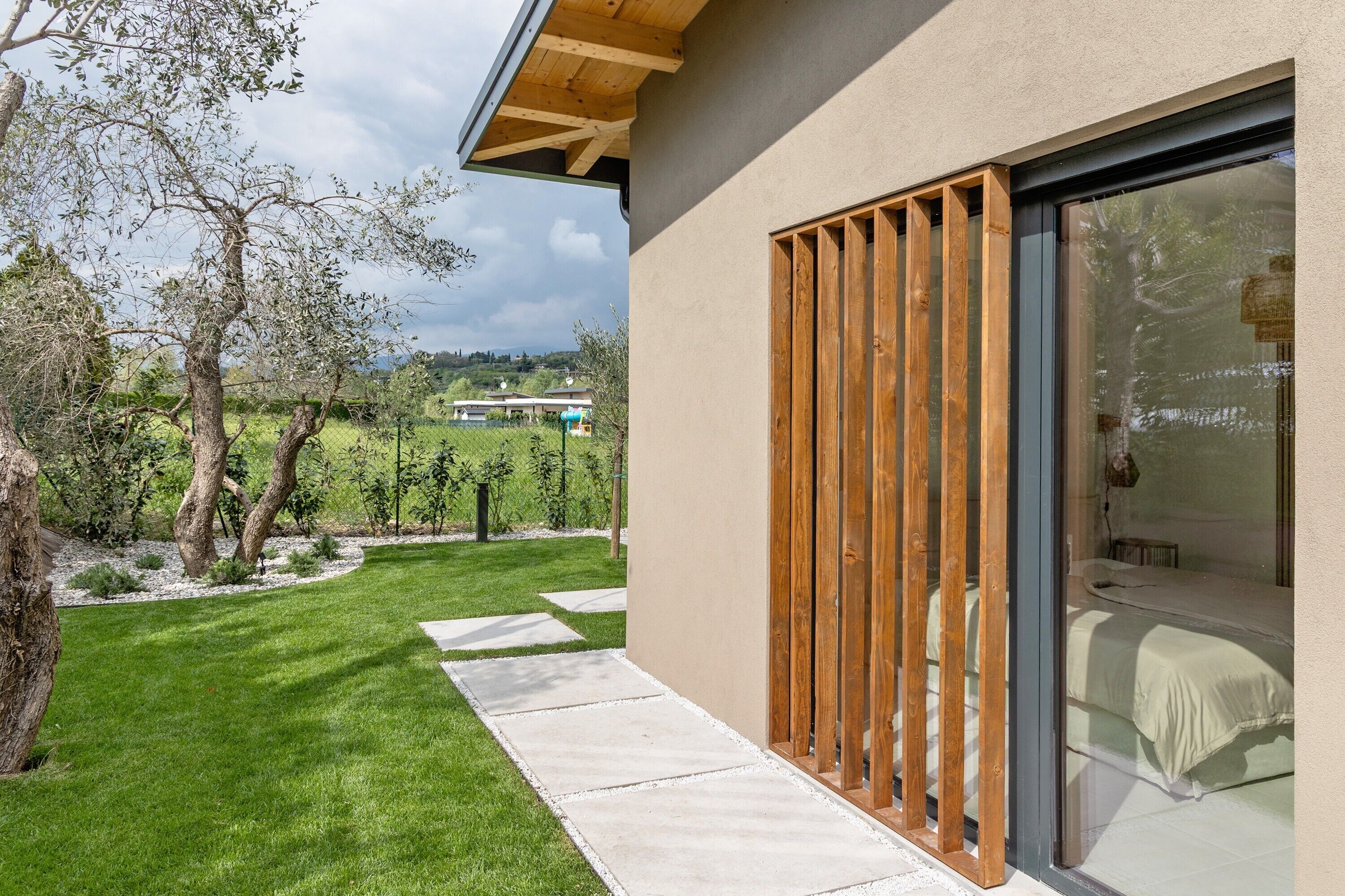 Un edificio moderno con puerta de cristal, ventana de listones de madera y césped cuidado con piedras para pisar.