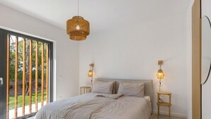 Ein Schlafzimmer mit einem großen Bett, zwei Nachttischlampen, einer Pendelleuchte und einer Glastür zum Garten.