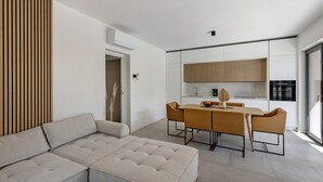 Ein modernes Wohnzimmer mit einer Eckcouch, einem Esstisch mit Stühlen und einer Küchenzeile mit Schränken und Geräten.