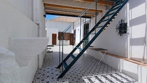 A narrow corridor with a tiled floor, a wooden door, and a blue staircase leading to an upper level. - Room 'Quarto 1' with Shared Terrace, Wi-Fi and Air Conditioning (Faro)