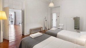 A hotel room with two beds, a bench, a mirror, a hanging light fixture, and a wardrobe.