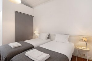 A hotel room with two single beds, a bedside table with a lamp, and a window with a blind. - Room 'Quarto 6' with Shared Terrace, Wi-Fi and Air Conditioning (Faro)