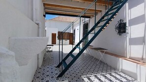 A narrow corridor with a tiled floor, a wooden door, and a blue staircase leading to an upper level.