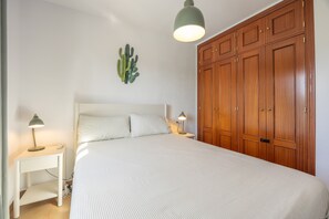 Une chambre à coucher avec un lit, des tables de chevet avec des lampes, une armoire en bois et une décoration murale représentant un cactus.