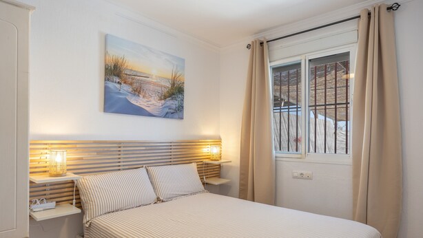 Un dormitorio con cama, lámparas de noche, un cuadro y una ventana con cortinas.