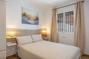 Ein Schlafzimmer mit einem Bett, Nachttischlampen, einem Gemälde und einem Fenster mit Vorhängen.