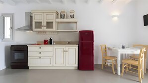 A kitchen with a stove, oven, cabinets, a red refrigerator, and a dining area with chairs and a table. - Apartment at 'Echinousa Kimolos Maisonette no3' Hotel with Sea View, Wi-Fi, and Air Conditioning (Psathi)