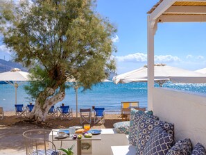 A seaside terrace with outdoor seating, a table set for breakfast, and umbrellas providing shade.