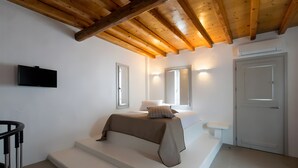 Ein Schlafzimmer mit einem Bett, einer Bank, einem Fernseher und einer Tür.