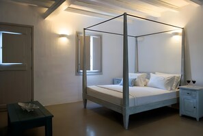 Un lit à baldaquin avec une literie blanche, une table de chevet avec un tiroir et une petite table sur laquelle est posé un objet décoratif.