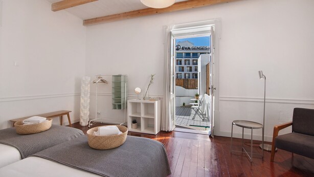 A room with two beds, a small table, a chair, a floor lamp, and a view of a building through an open door. - Room '8' with Shared Terrace, Wi-Fi and Air Conditioning (Faro)