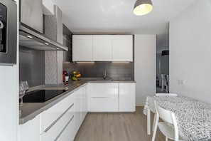 Une cuisine moderne avec des meubles blancs, une cuisinière encastrée et un coin repas agrémenté d’une nappe à motifs.
