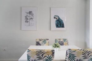 Un comedor con una mesa blanca, sillas estampadas y dos obras de arte enmarcadas en la pared.