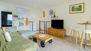 A living room with a sofa, a TV, a wooden cabinet, a small table, and a bar area with stools. - Mediterranean Escape Between the Sea and the Esterel Mountains (Théoule sur Mer)