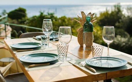 A table set with plates, glasses, and cutlery, with a bottle and decorative basket on the table, overlooking a scenic view.