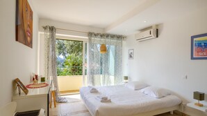 A bedroom with a bed, a nightstand, a lamp, a window with curtains, and an air conditioning unit. - Mediterranean Escape Between the Sea and the Esterel Mountains (Théoule sur Mer)