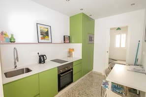 A kitchen with green cabinets, a white countertop, a sink, a stove, and a microwave.