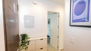 Un corridoio con una porta in legno, una pianta, un quadro incorniciato e un'apertura che dà su un'altra stanza.
