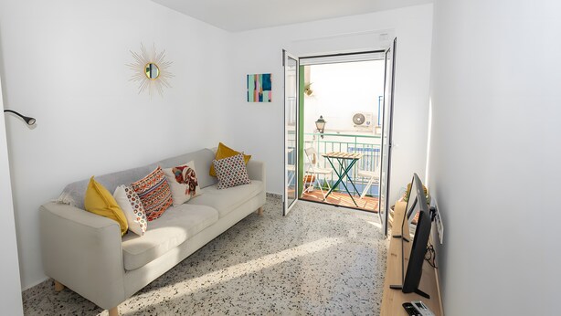 Un soggiorno con divano, televisione e balcone con mobili da esterno.