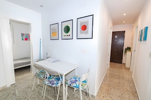 A room with a white table, two patterned chairs, a framed abstract art piece, and a door with a sign.