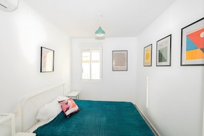 A bedroom with a bed, a bedside table, a window, and framed artwork on the walls.