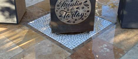 Ein Metalltisch mit einem Schild, auf dem 'Le Moulin de Tartay' steht, auf einer gefliesten Terrasse.