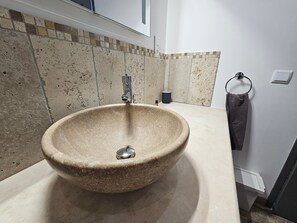 A bathroom with a large stone sink, a towel ring, and a tiled backsplash.