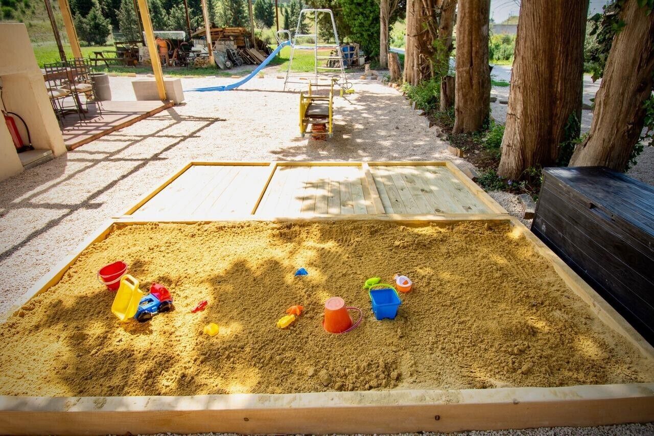 A sandbox with toys, a slide, and a swing set in an outdoor play area.