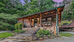 A rustic cabin with a stone foundation, wooden exterior, and a porch with string lights.